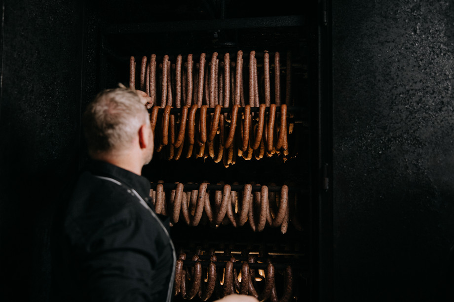 Man standing in front of the smoker with hung sausages