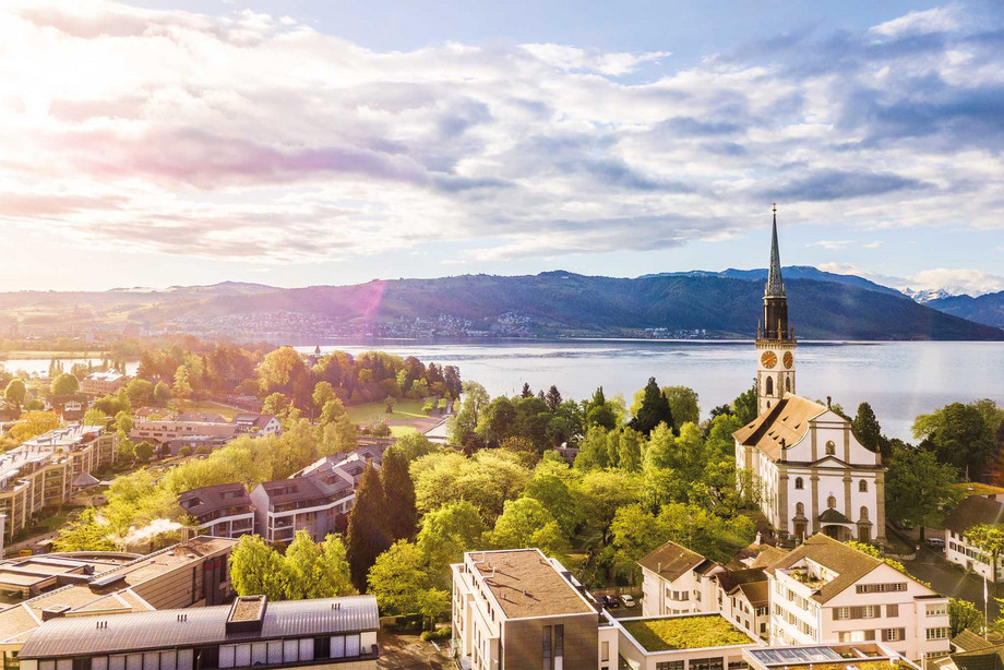 Flugaufnahme von Cham mit Kirchenturm und Zugersee im Hintergrund