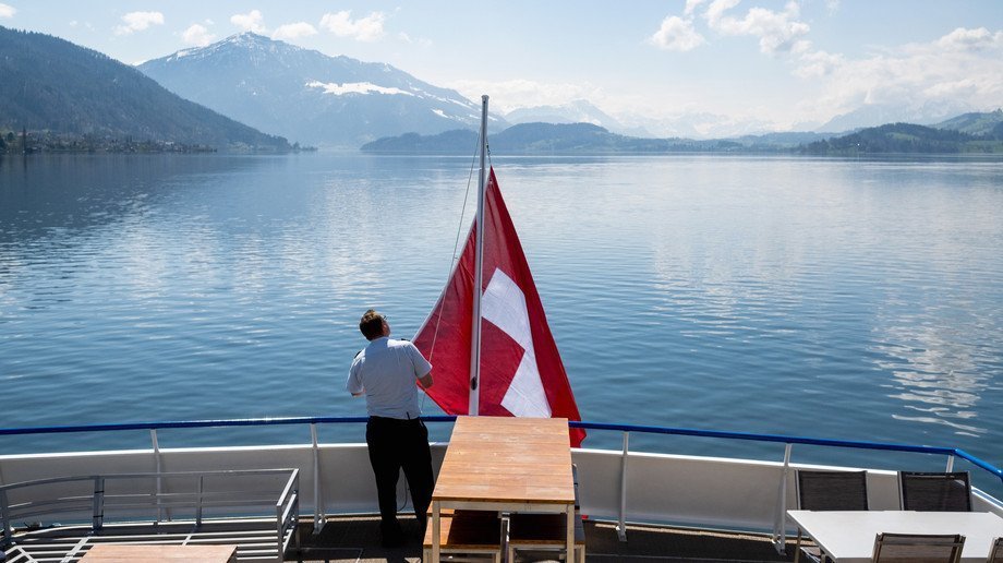 Flag hoisting Lake Zug Sailor hoisting the Swiss flag on the stern with a view of the lake