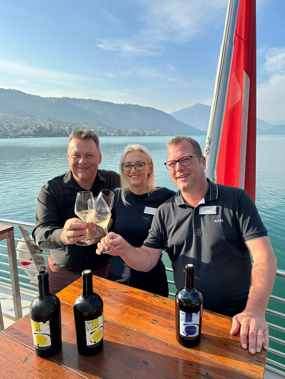 Drei Personen stossen mit Gastronautic-Wein an, im Hintergrund ist der See